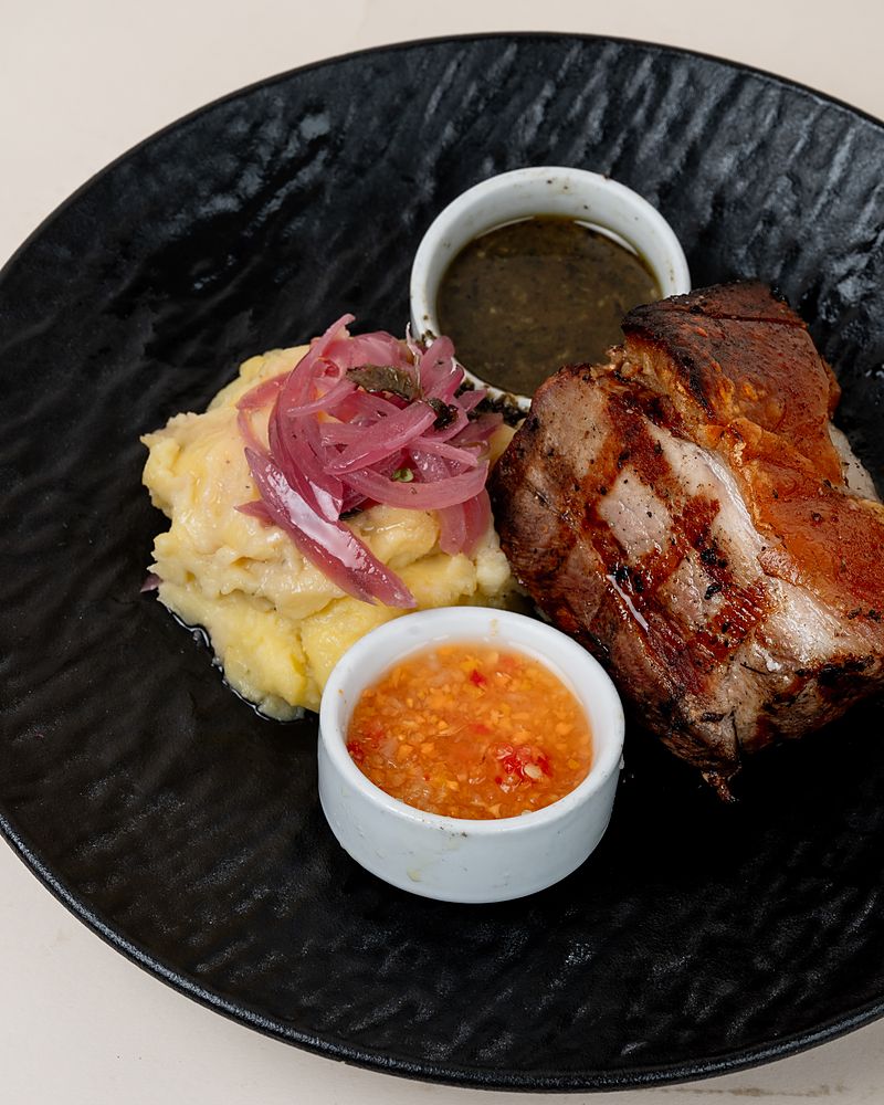 Lechón de la Abuela servido en plato de barro con puré y cebolla encurtida