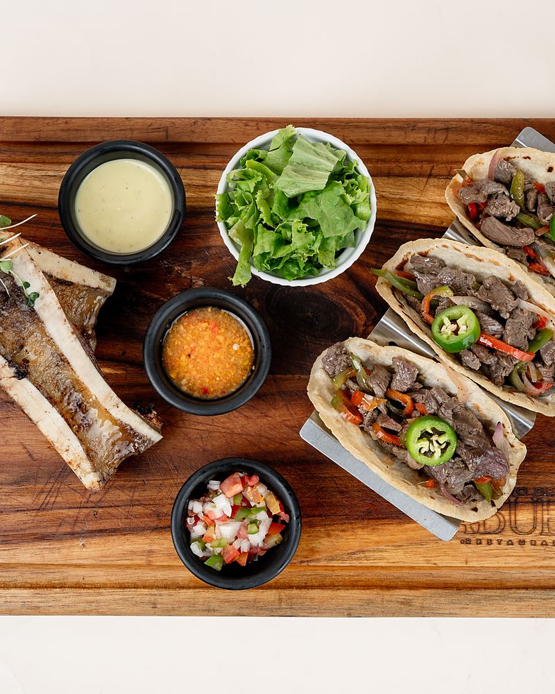 Tacos de tuétano sobre tabla de madera con salsas y pico de gallo