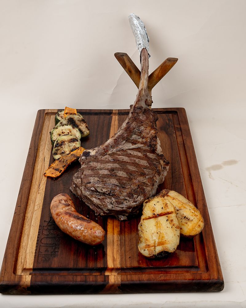 Corte Tomahawk servido en tabla con chorizo y plátano asado
